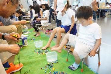 足でビー玉をつかむミニゲームをする子どもたち