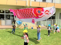 子ども達が、園庭に飾られた鯉のぼりに触れて遊んでいます。