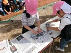 子どもが芋を新聞で巻いています。