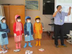 赤、青、黄色の雨具をみにつけいる子ども4人と講師