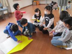 黄色の1メートル四方の折り紙を折る子ども