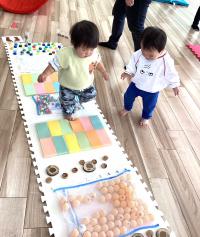 マットの上を歩く子どもとそれを側から見ている子どもの画像