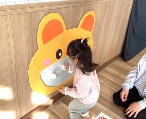 壁に貼っているくまの口にボールをくっつけている児の画像