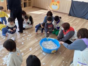 床に散らばっている紙の素材の雪をみんなでかたづける画像