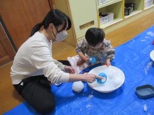 保育士と一緒に雪を触っている画像