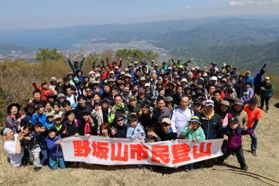 山頂で、「野坂山市民登山」と書かれた横断幕を持ち、多くの参加者が集合写真を撮っている