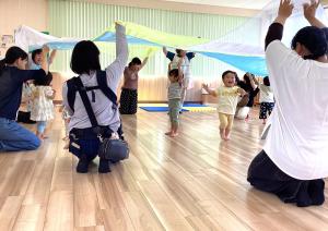 大きなオーガンジーの布で遊ぶ親子たちの画像