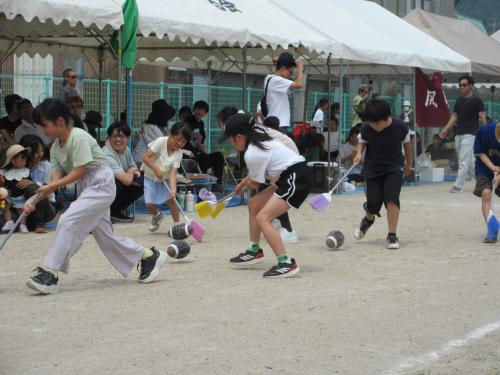 障害物競走で、小学生がほうきでラグビーボールを運んでいる画像