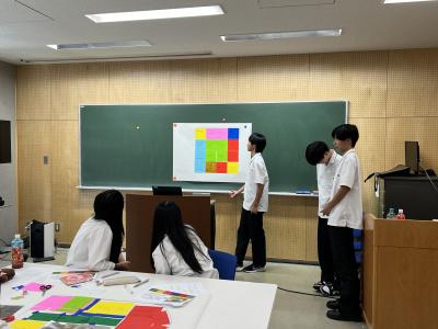 模造紙を見ながら提案を説明する制服を着た学生の画像