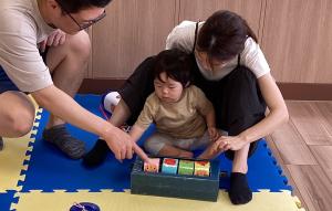 父と母と手作り玩具で遊ぶ男児の画像