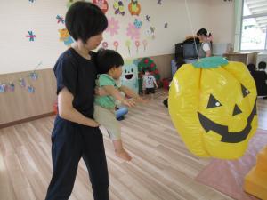 母親に抱かれ、かぼちゃの風船にタッチしようとする男児