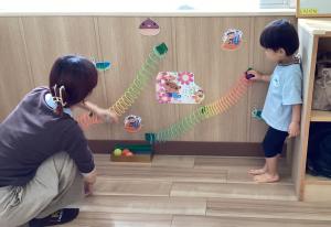 ボールを転がす玩具で遊ぶ男児と母