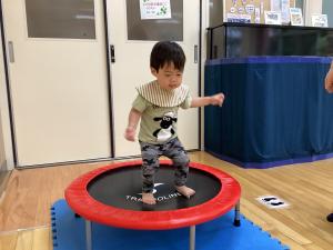緑色の服を着た子どもがトランポリンを飛んでいる様子