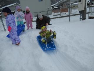 雪が積もった園庭でソリ遊びをしています。