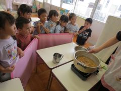 夏野菜カレークッキングの様子。みんなで鍋にルーを入れるところを見ています。