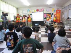 オレンジ色のユニフォームを着た猟友会の皆さんの話を聞いている子供たち