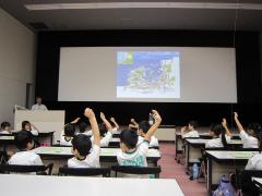 大きなスクリーンを見ながら挙手する子供たち