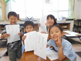 文字を書いたA4サイズの紙を持って笑顔の子ども4人