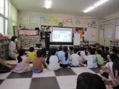 スクリーンの前で手話を教える講師と座って話を聞く子どもたち