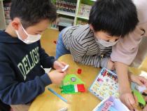 折り紙の本を見てみんなで折り紙を折る子どもと職員