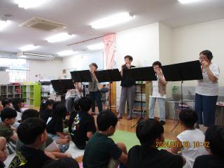 黒い譜面台の奥にオカリナを演奏する人達と座って聞く子どもたち