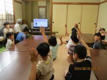 テレビ画面のクイズに手をあげて答える子どもたち