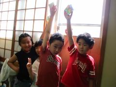 窓際で工作した宝石箱を太陽光にかざす子ども4人