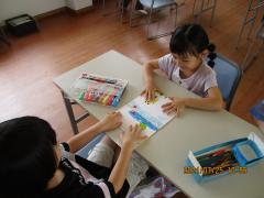 机の上に色紙をおいてマジックペンで絵を描く子ども