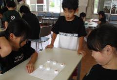 白い紙の上にペットボトルキャップを並べて遊ぶ子どもたち