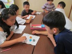 白い紙の上に色とりどりのペットボトルキャップを並べて対戦する子ども