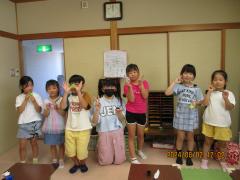 折り紙のカエルを手に持ちポーズをとる子ども